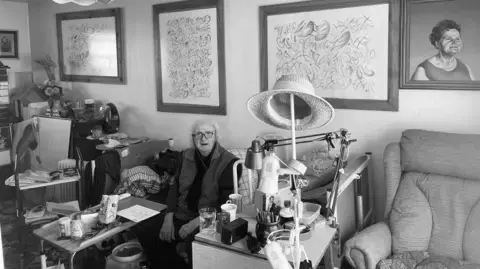 عکس سیاهسفید وینسور بیرچ از هنری اورلیک در دههٔ ۷۰؛ او در یک اتاق نشیمن نشسته، پشت سرش نقاشیهای قابدار و یک مبل در سمت راست