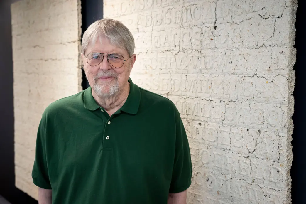 جیم سنبورن، هنرمند مجسمه کریپتوس، در مقابل اثر هنری خود که از خمیر اسناد سازمان سیا ساخته شده، ایستاده است.