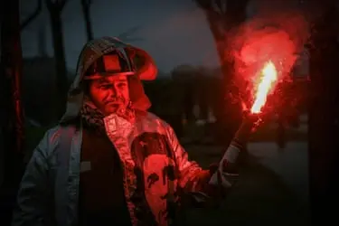 مردی در تاریکی که توسط مشعلی که در دست دارد روشن می‌شود