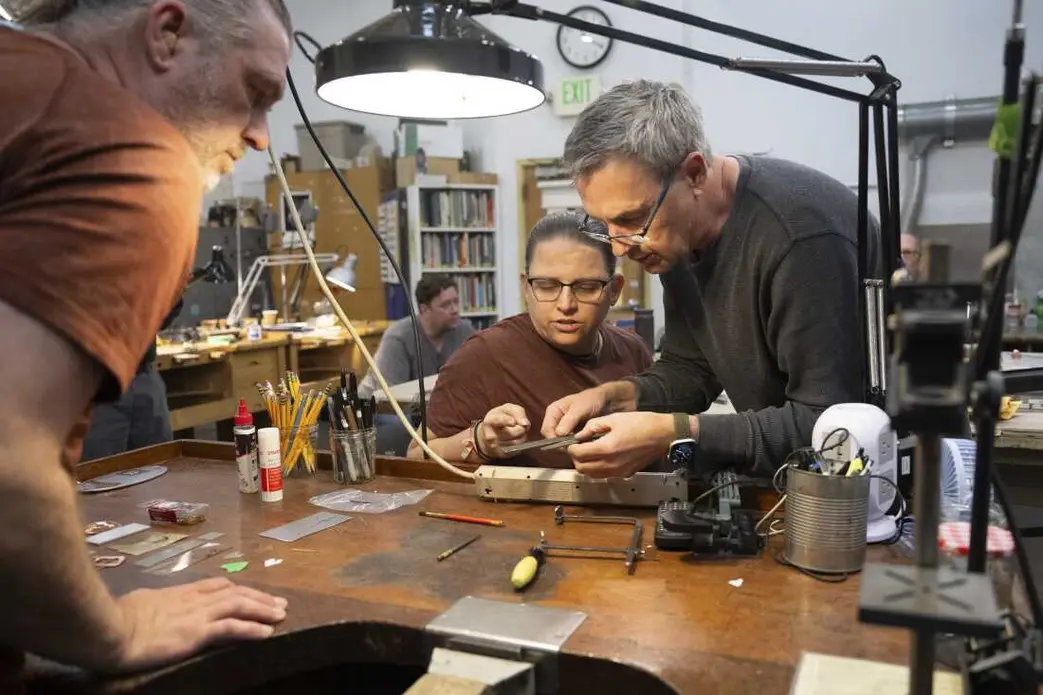 زره موشی جِف دی بوئر و چند ابزار حرفه‌ای روی یک میز کار در مرکز هنرهای زیبا پرات در سیاتل، واشنگتن، در تاریخ ۹ اکتبر ۲۰۲۵ چیده شده‌اند.