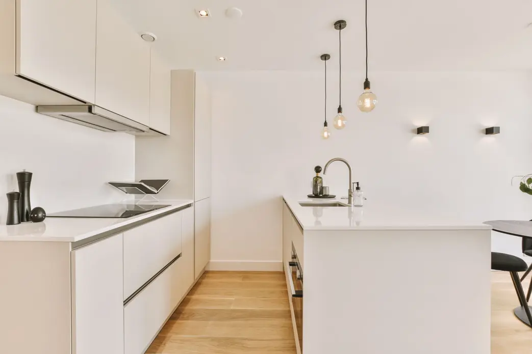 آشپزخانهای کوچک با دکور سفید و کفپوش پارکت در یک خانهٔ دلپذیر