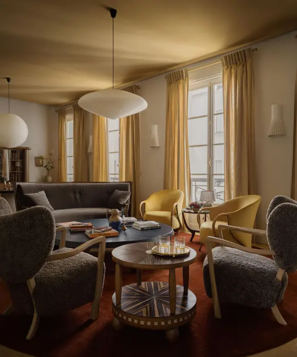 اتاق نشیمنی با سقف ارچ، دیوارهای سفید گرم و پنجره بزرگ با پرده‌های ارچ. فرشی قرمز تیره و صندلی‌های خنثی تاریک